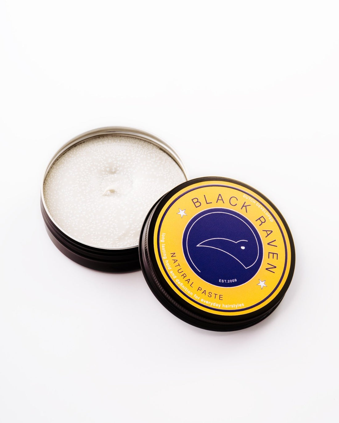 Black Raven Natural Paste for hairstyles, providing long-lasting hold and definition. Round yellow tin with a raven logo.
